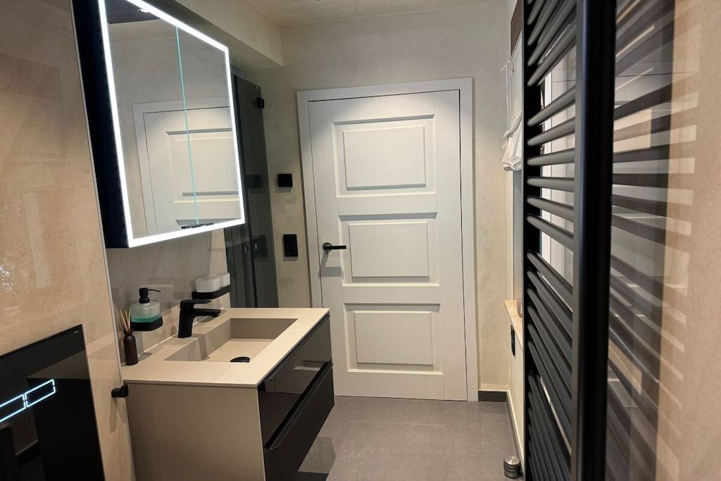 A modern bathroom with a sink, mirror, and a door with a handle.
