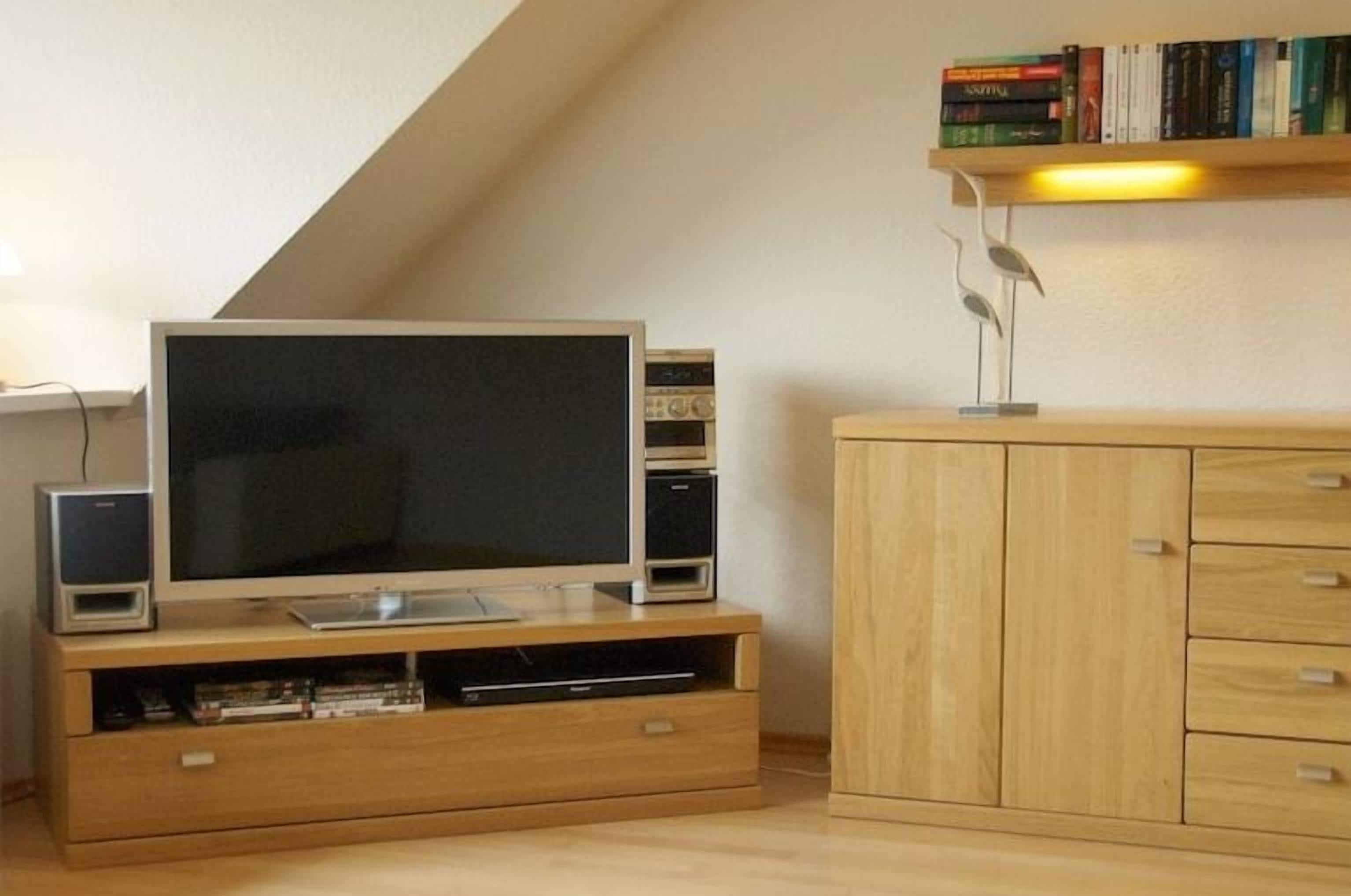 Une pièce comprenant un téléviseur posé sur un meuble en bois, une bibliothèque et un meuble avec des tiroirs.