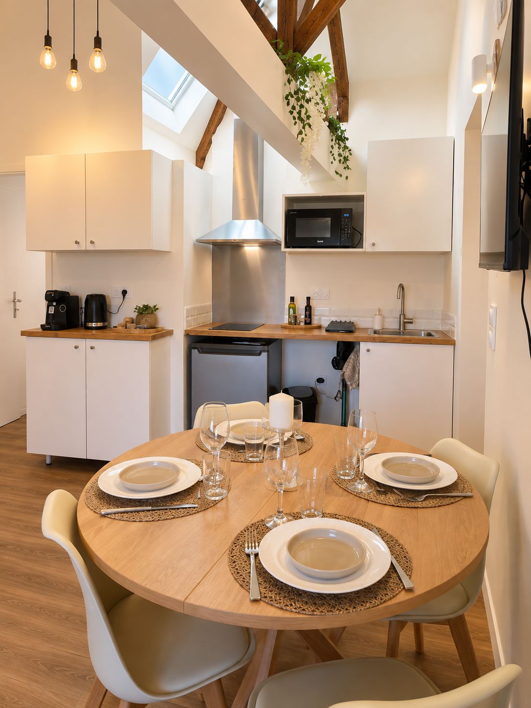 Una cocina moderna con armarios blancos, una campana extractora de acero inoxidable y un comedor con una mesa redonda para cuatro personas.
