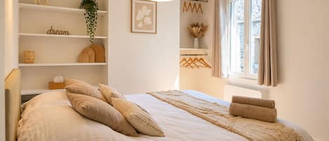 Una camera da letto con un letto grande, un comodino, una lampada a sospensione, una finestra con tende e una mensola con oggetti decorativi.