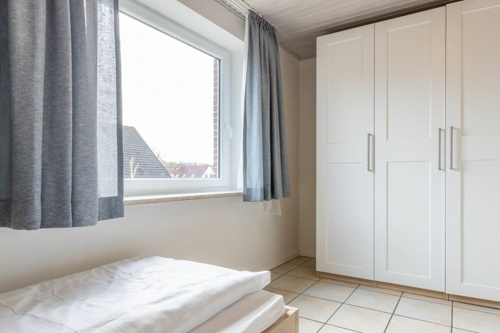A bedroom with a bed, a window with curtains, and a wardrobe.