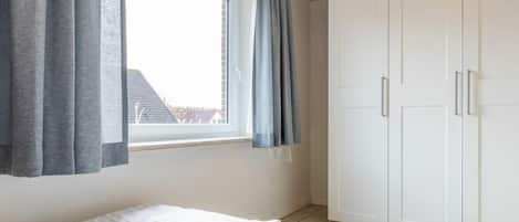 A bedroom with a bed, a window with curtains, and a wardrobe.