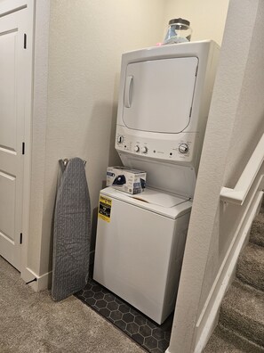 A compact laundry room with a front-loading washer and dryer, a towel rack, and a carpeted floor.