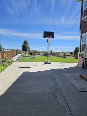 A basketball hoop on a concrete patio with a clear sky and a grassy area in the background.