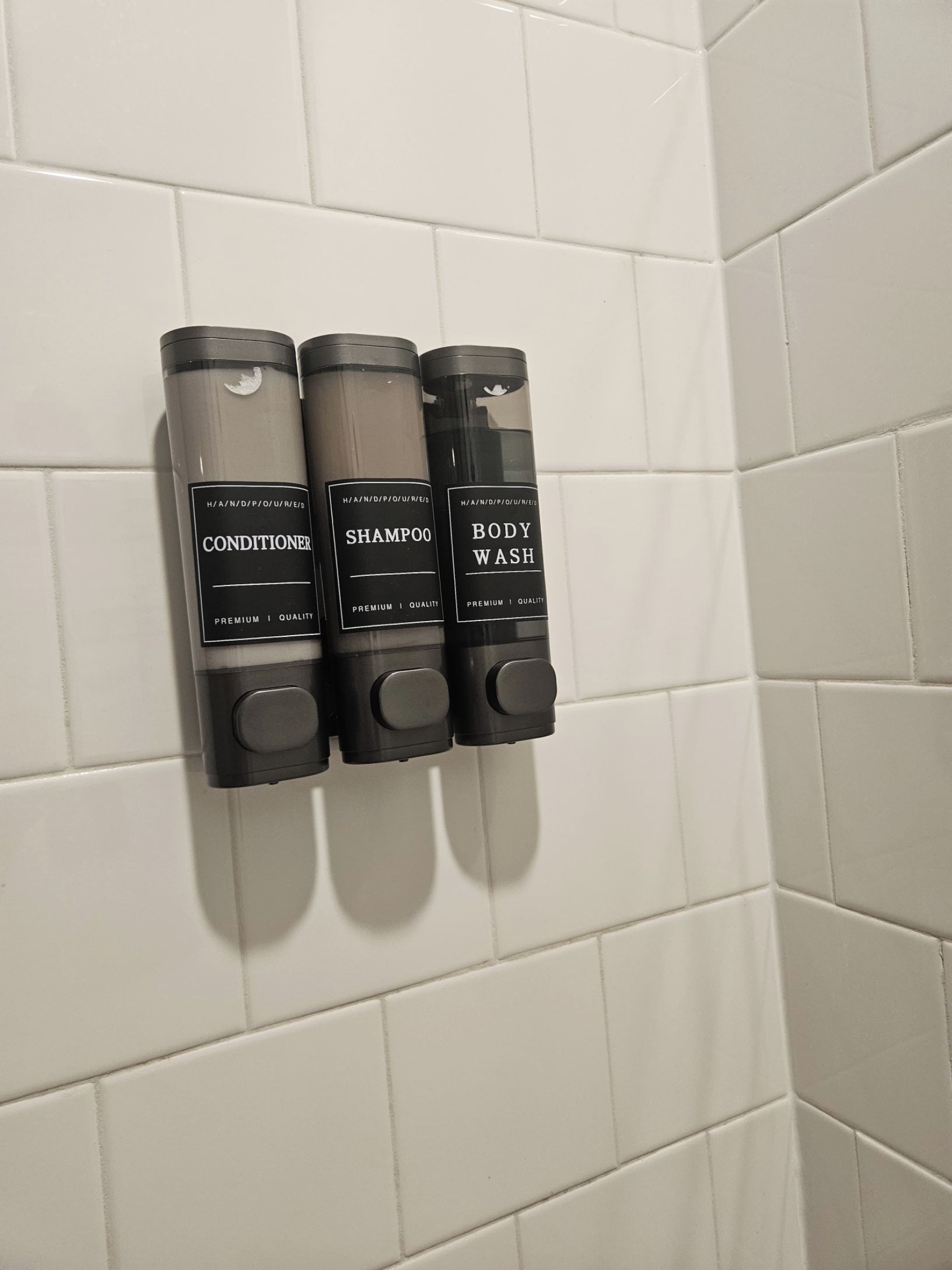 A set of three toiletries in a bathroom with white tiled walls.