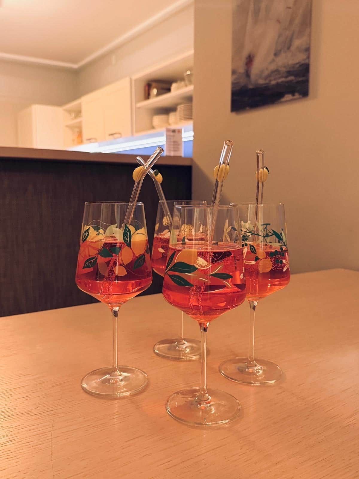 Three glasses of red beverage with fruit garnishes on a wooden table in a restaurant setting.