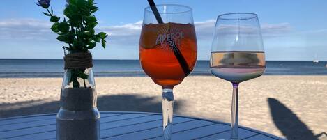 A table with three glasses of beverages and a small plant on a beach.