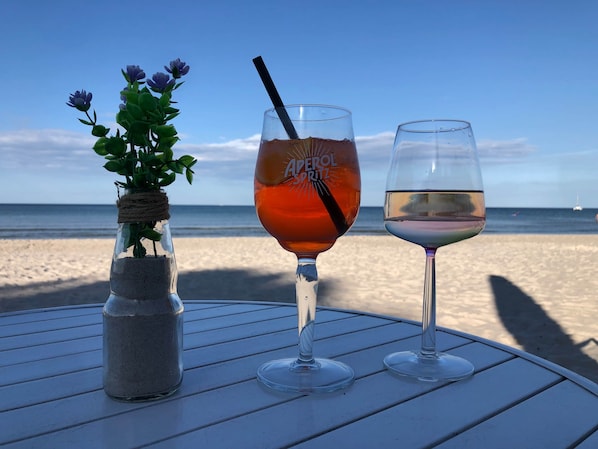 A table with three glasses of beverages and a small plant on a beach.