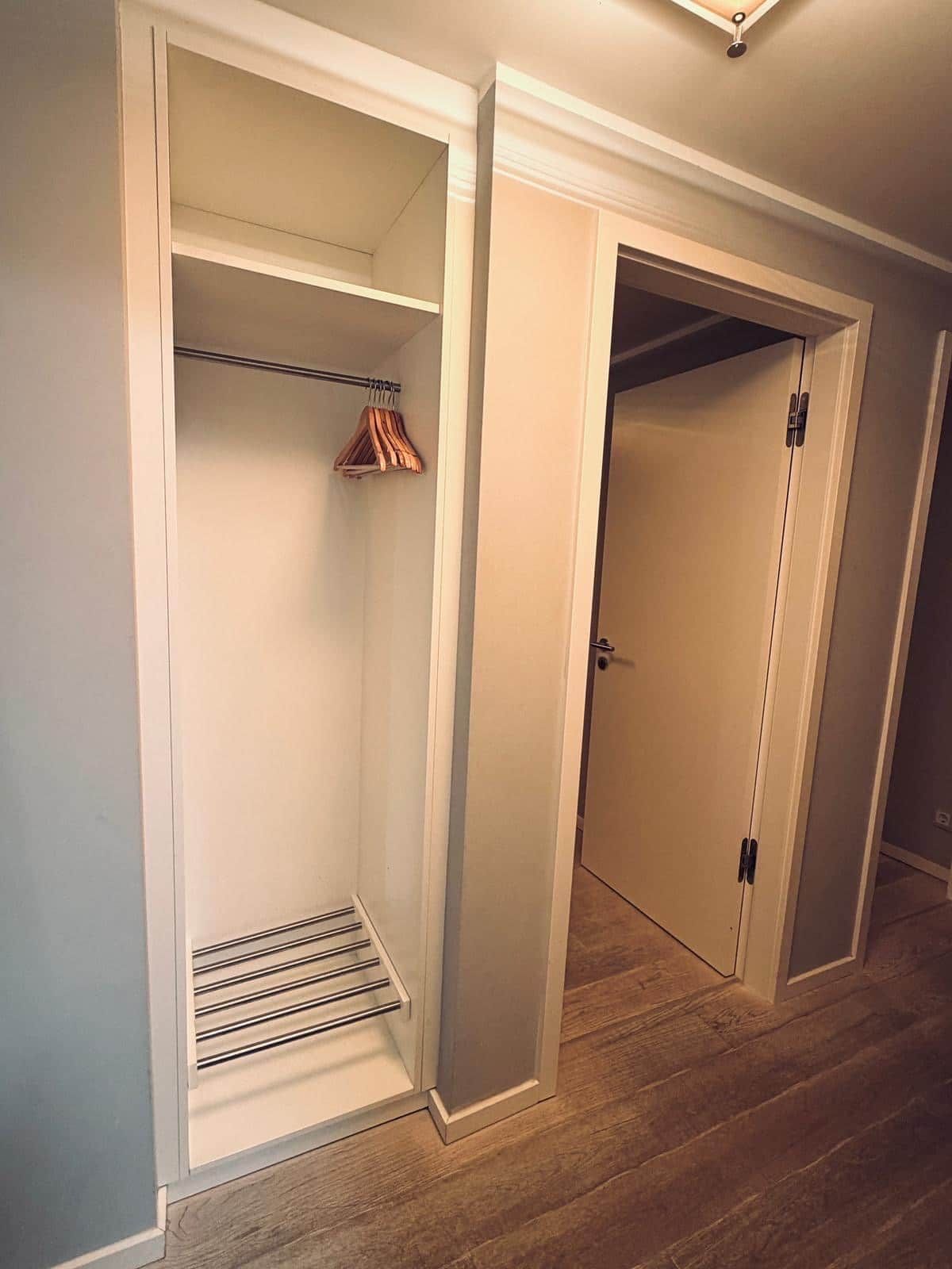 A walk-in closet with a metal rod and wooden hangers, a door with a handle, and a wooden floor.