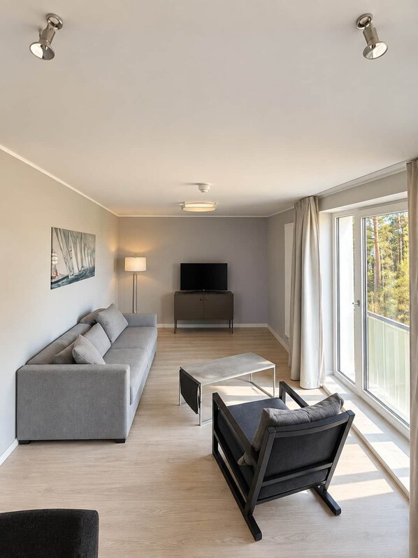 Un salon moderne avec un canapé, une table basse, un meuble pour la télévision et une grande fenêtre avec des rideaux.