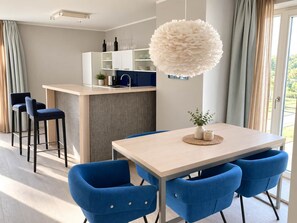 A modern kitchen with a central island, bar stools, a dining table with blue chairs, and a decorative white spherical light fixture.
