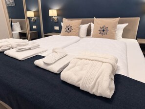 A hotel room with a neatly made bed, towels, slippers, and a headboard with decorative pillows. - Prora Select Vacation Rental in Prora for up to 5 people (Binz)