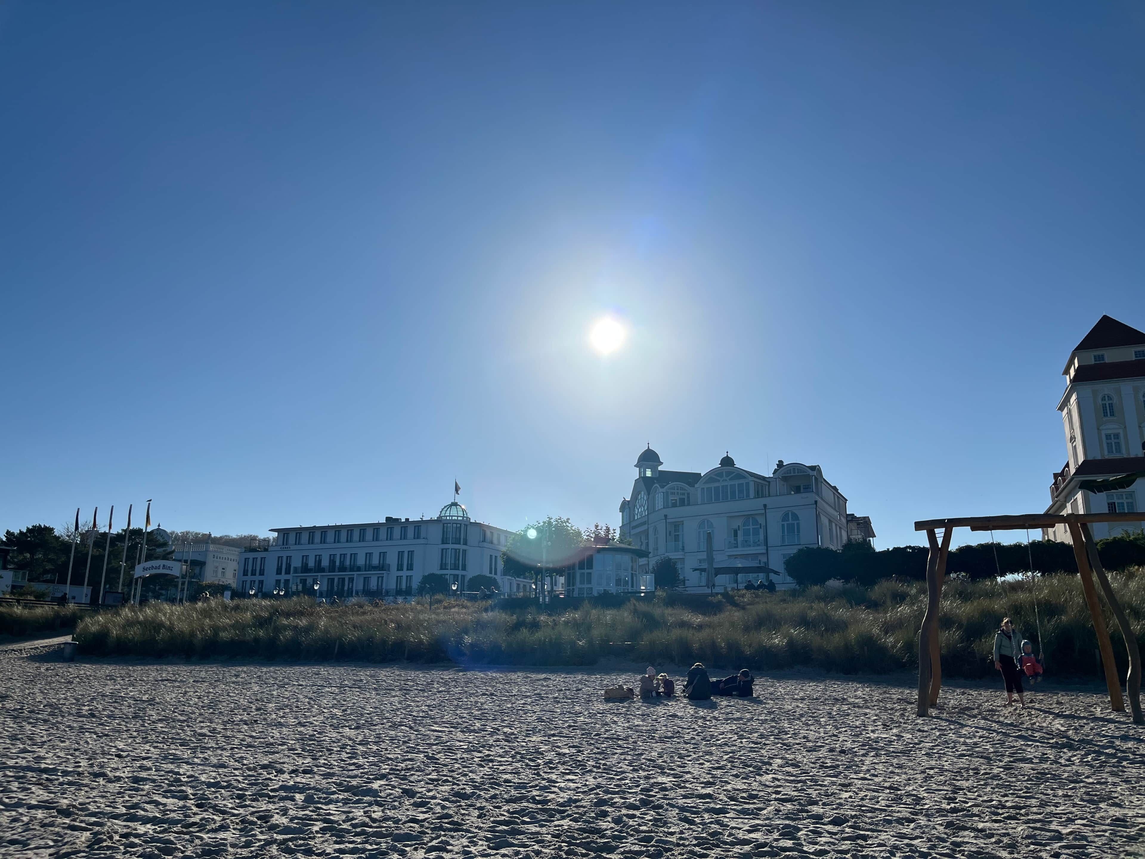 A sandy beach with a large building in the background and a swing set on the right.