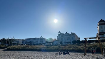 A sandy beach with a large building in the background and a swing set on the right.