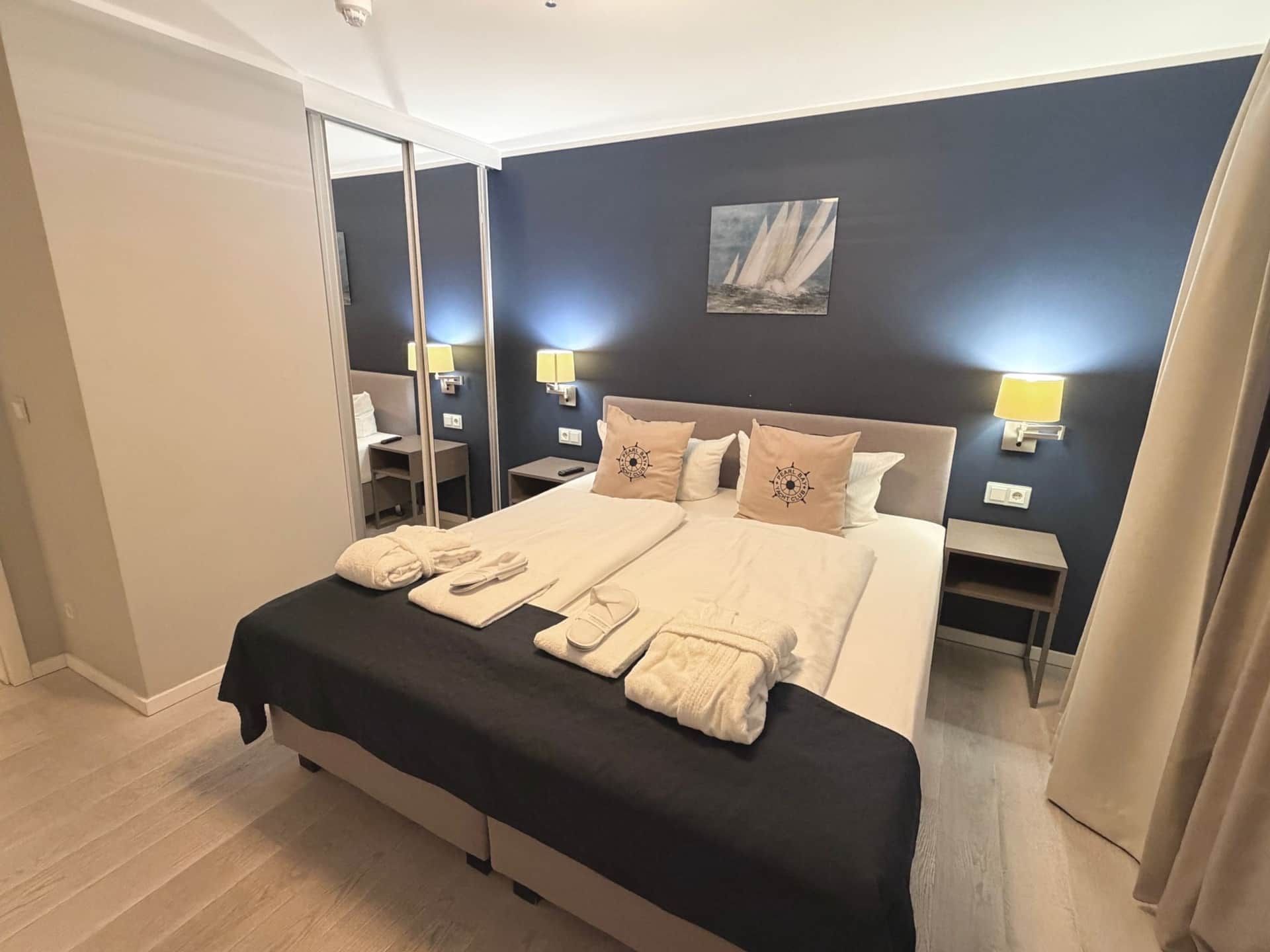 A hotel room with a large bed, two bedside tables, a mirror, and a painting on the wall.