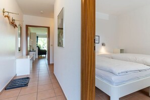 A hotel room with a bed, a desk, and a chair. There is a door leading to another room. - Villa Anna II, Apartment 71 (St. Peter - Ording)
