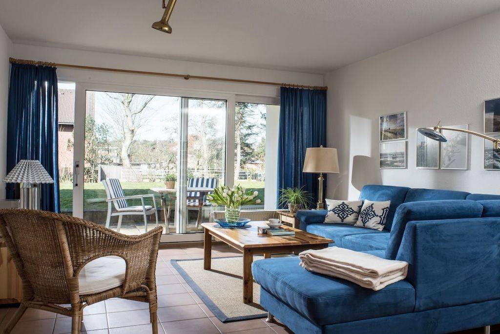 A living room with a blue sofa, a wicker chair, a coffee table, and a view through a glass door to an outdoor area.