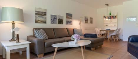 A modern living room with a sofa, coffee table, and a dining area with chairs and a table.