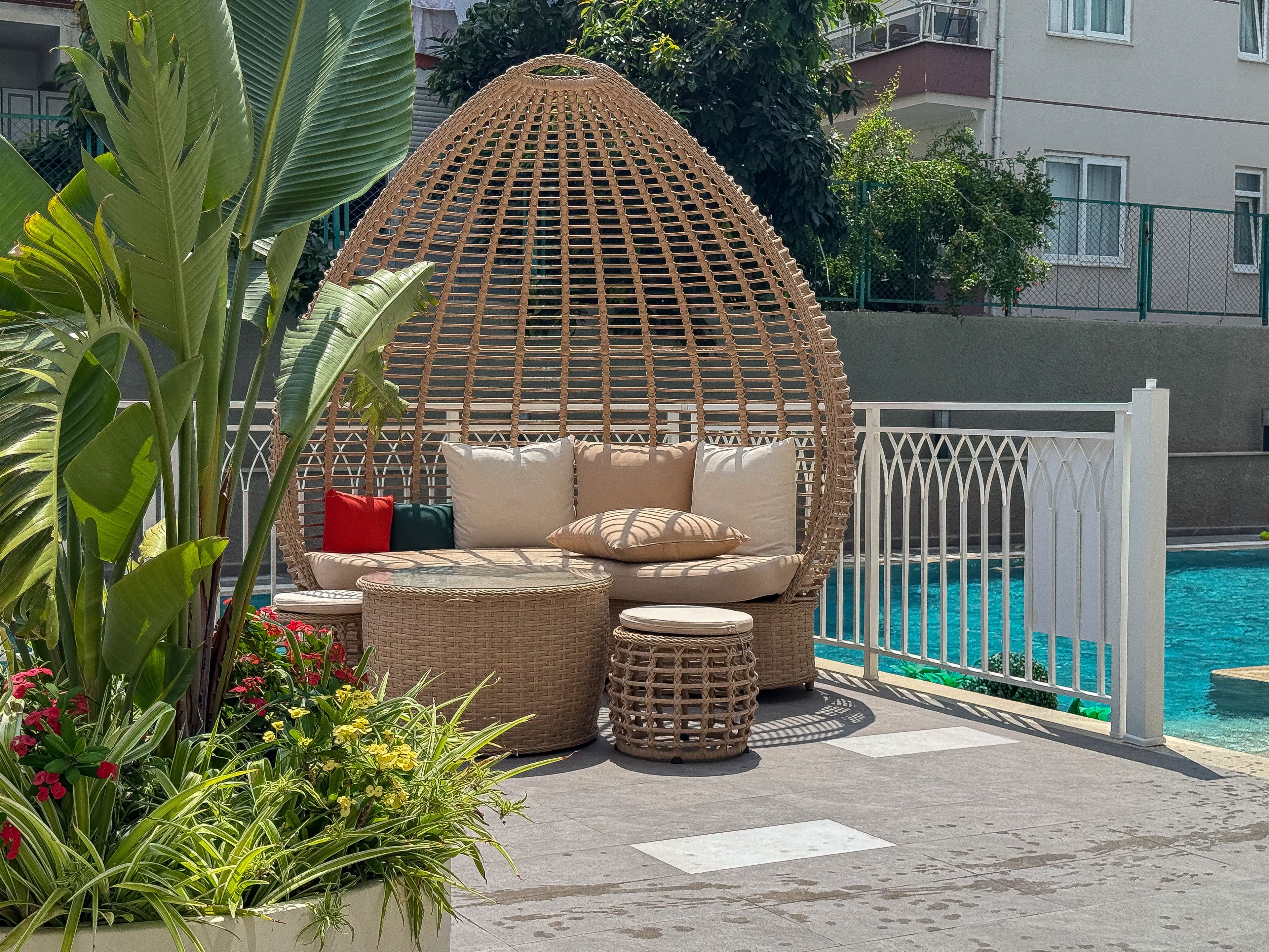 A wicker lounge chair with cushions, a small round table, and a pool in the background.