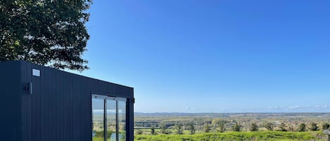 A modern building with large windows, a grassy lawn, and a view of distant hills.