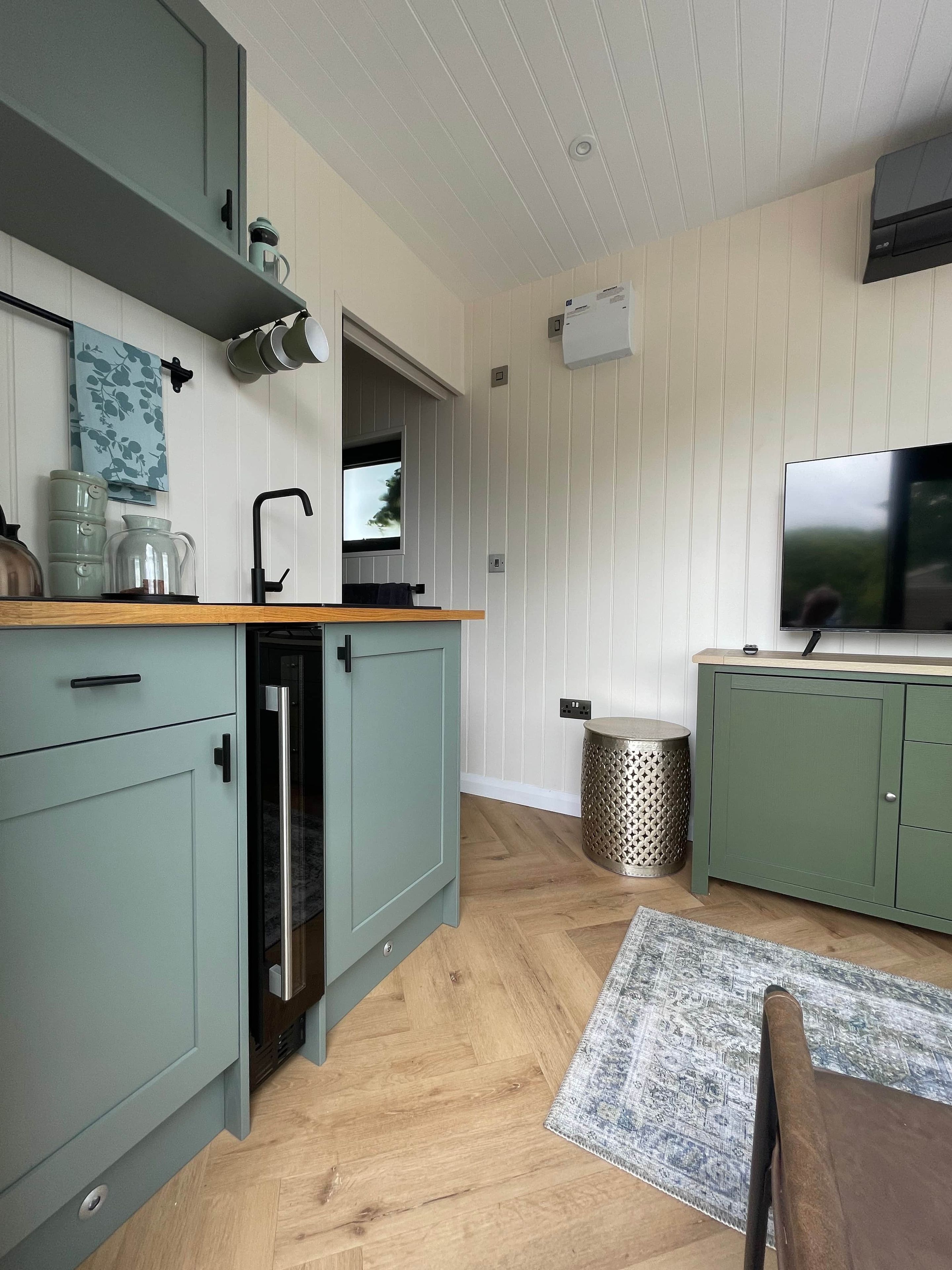 A compact kitchen with a built-in dishwasher, a window, and a flat-screen TV.