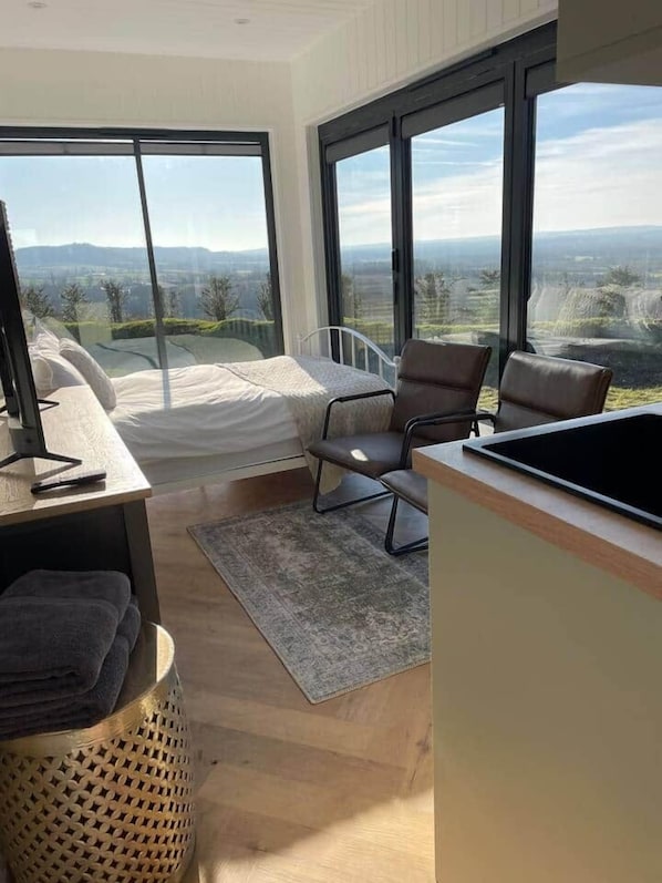 A modern bedroom with a large bed, a desk, and a view of the countryside.
