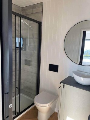 A bathroom with a glass-enclosed shower, a toilet, and a sink with a round mirror.