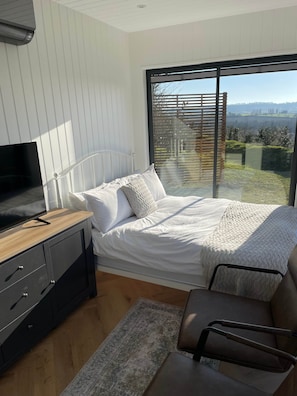 Un dormitorio con cama, televisión, escritorio y vistas al exterior.