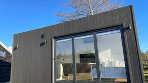 Een modern gebouw met grote glazen schuifdeuren, een donkere gevel en een zichtbare achtertuin.