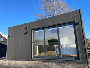 Un edificio moderno con grandes puertas correderas de vidrio, fachada oscura y un patio trasero visible.