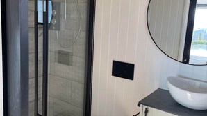 Een moderne badkamer met een glazen douchecabine, een wit toilet en een ronde spiegel boven een witte wastafel.