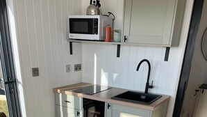 Een kleine keuken met een magnetron, spoelbak en een inbouwoven.