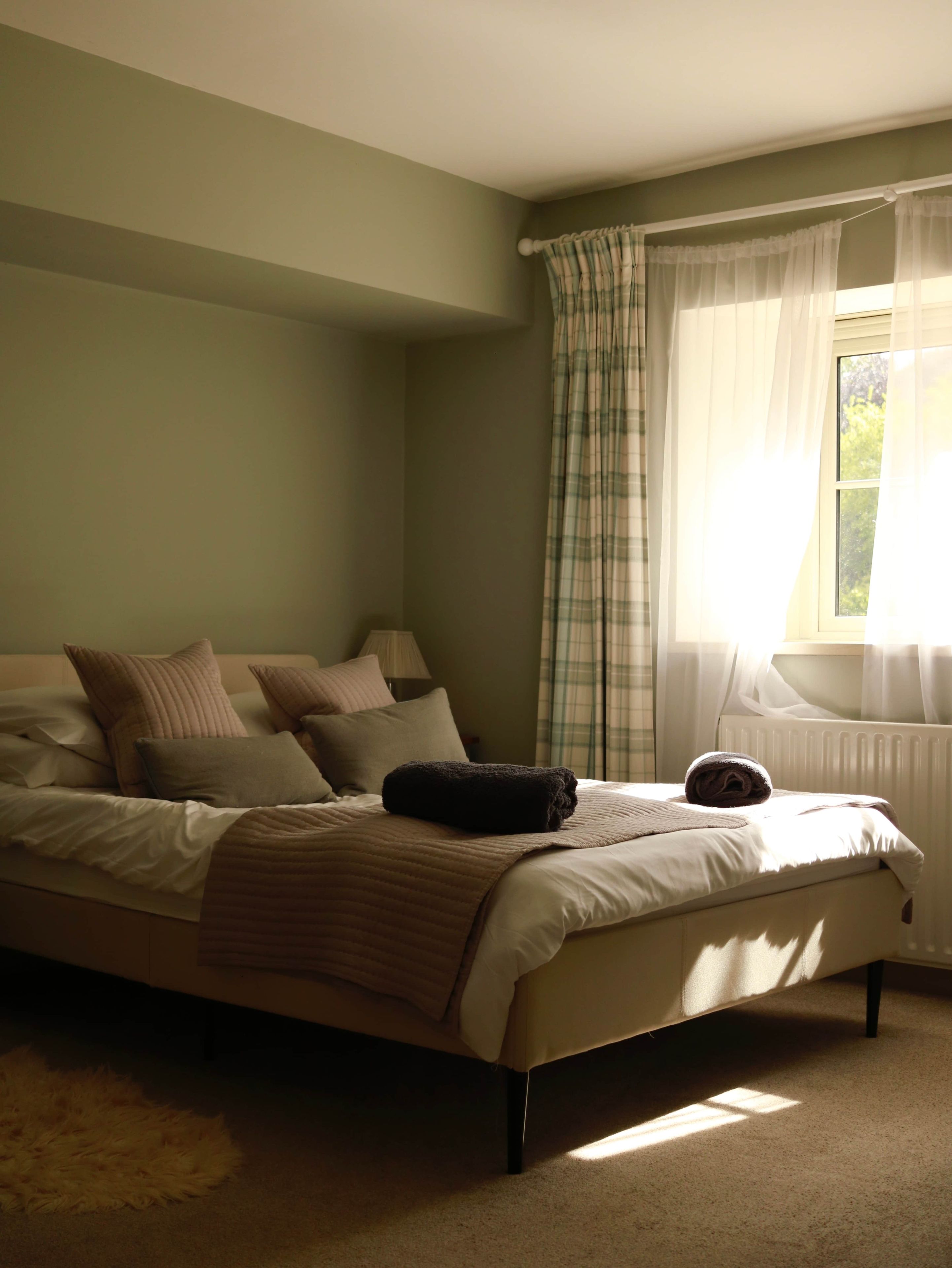 A bedroom with a bed, pillows, a blanket, a window with curtains, and a radiator.
