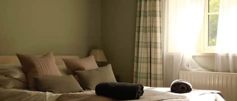 Un dormitorio con cama, almohadas, una colcha, una ventana con cortinas y un radiador.