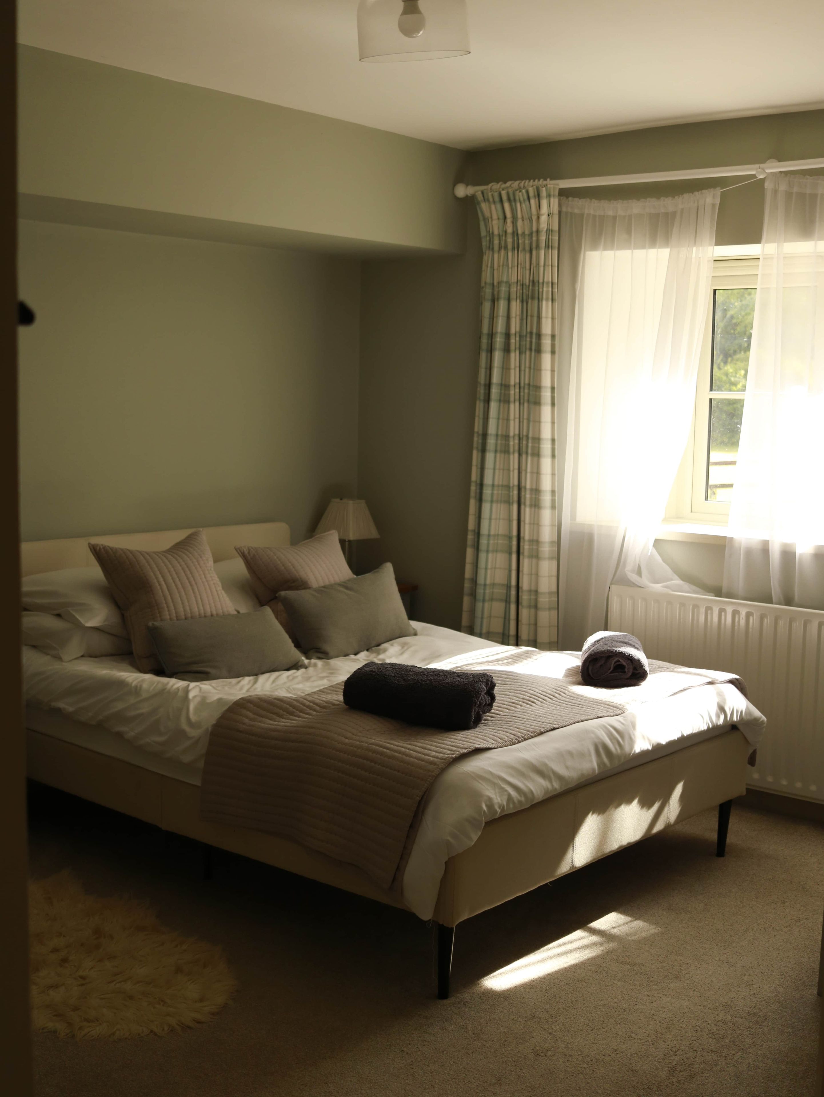 A bedroom with a bed, a lamp, and a window with curtains.