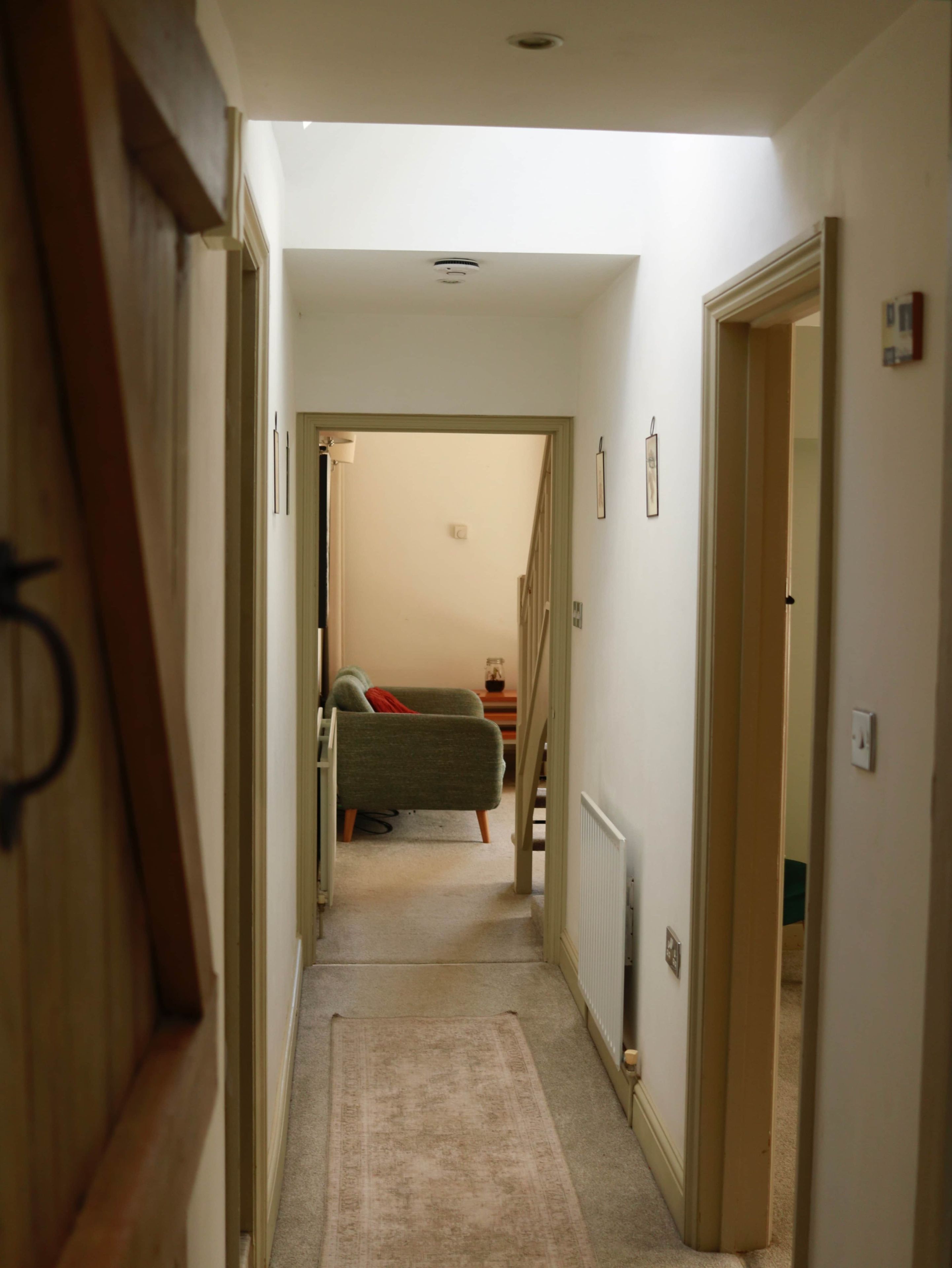 Corredor estreito com piso coberto por carpete, que leva a um quarto com cama e mesa de cabeceira.
