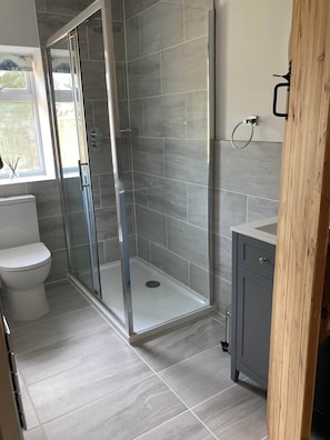 Un bany modern amb dutxa amb vidre, vàter i un lavabo amb detall de fusta.