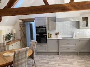 A kitchen with grey cabinets, a white countertop, and a wooden dining table with plaid chairs. - Cosy Barn Conversion with Stunning Views (Kings Langley)