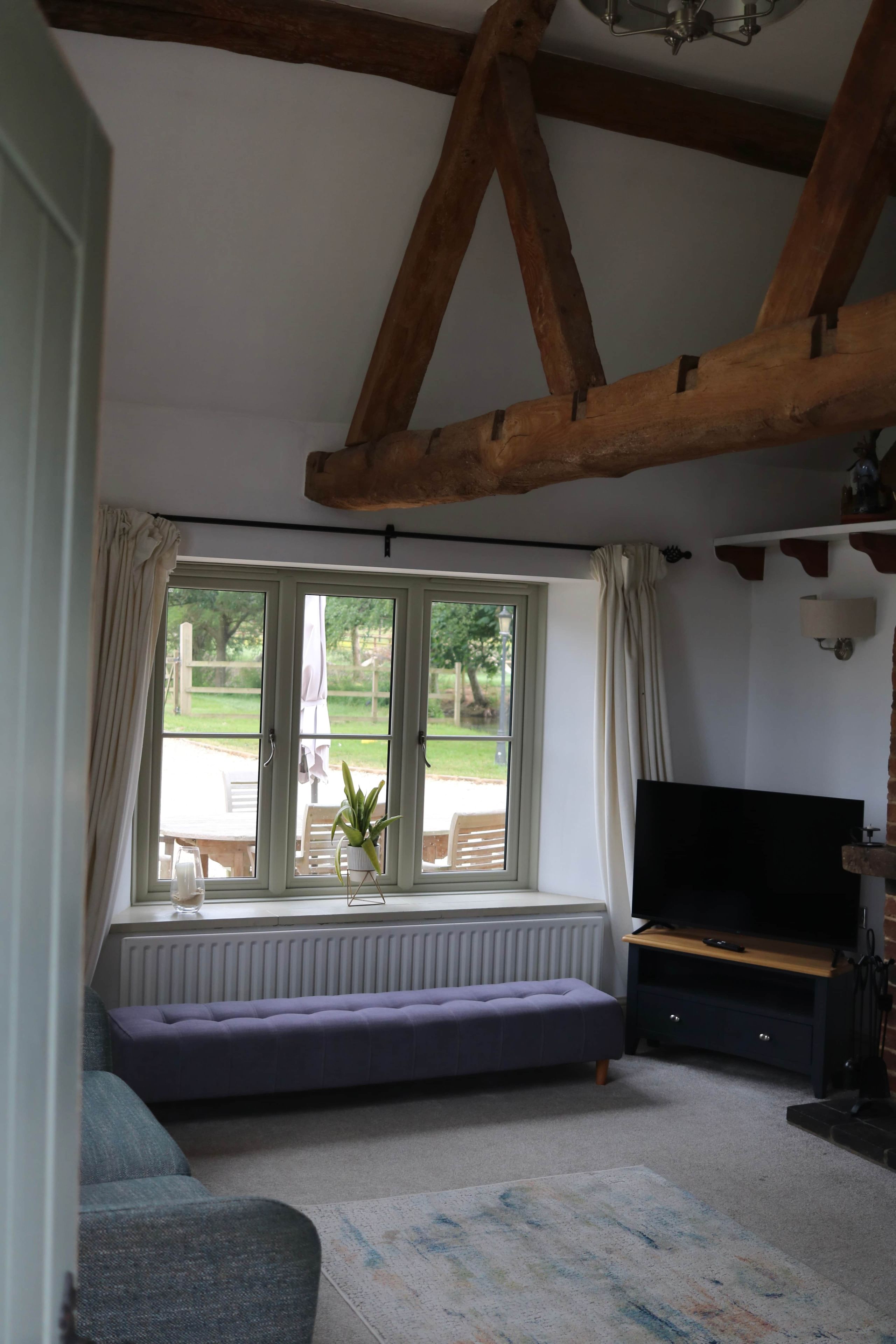 A living room with a large window, a sofa, a television, and a radiator.