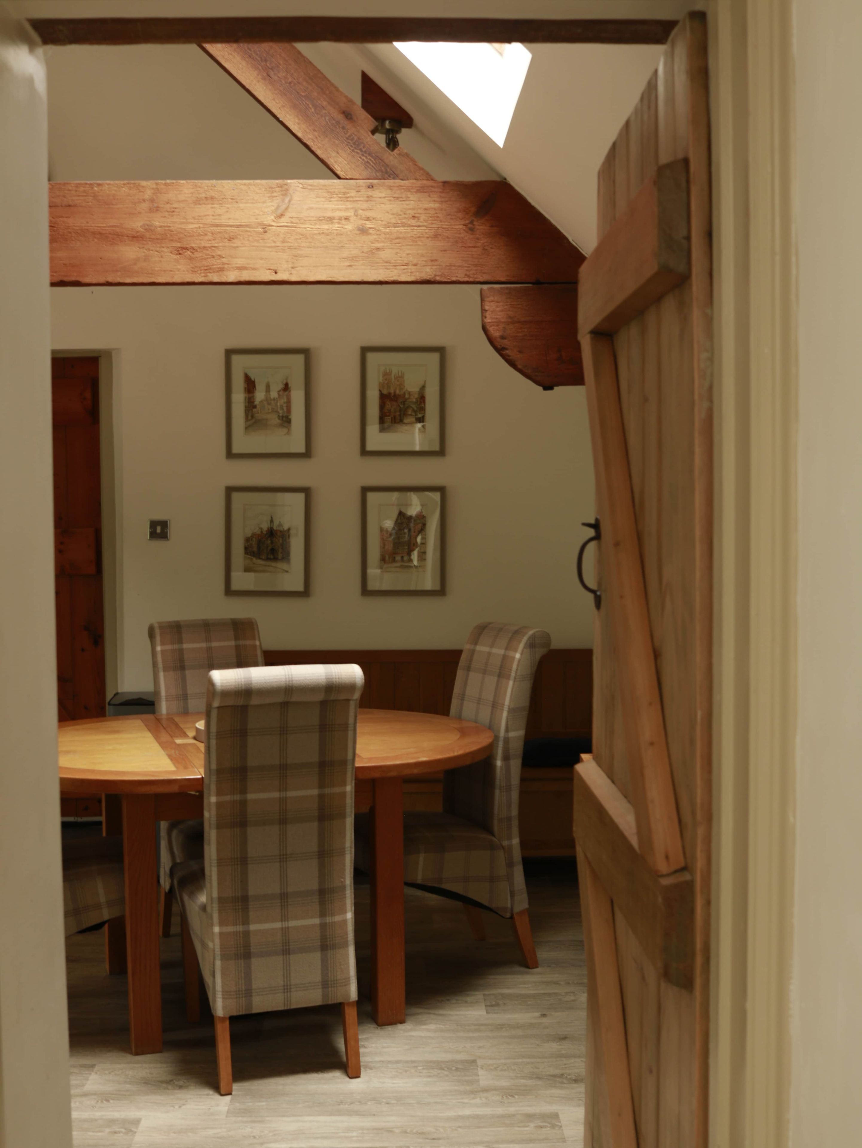 Un comedor con una mesa de madera y cuatro sillas, techo inclinado y cuatro cuadros en la pared.