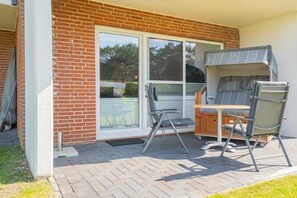 A patio with a table and chairs, a sliding glass door, and a brick wall. - 2 in the Utlande house (ID 086) (St. Peter-Ording)