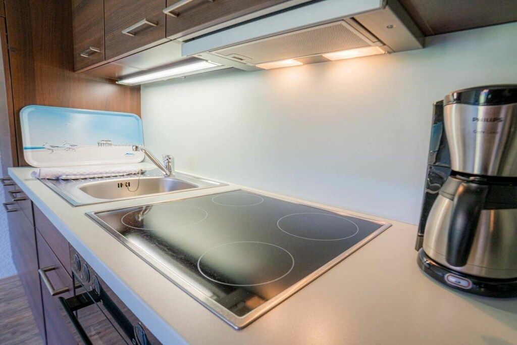A compact kitchenette with a stove, sink, and a coffee maker.