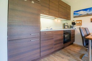 A modern kitchen with wooden cabinets, a built-in oven, and a dining area with a table and chairs. - 2 in the Utlande house (ID 086) (St. Peter-Ording)