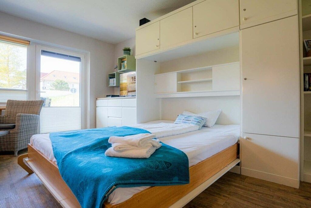 A room with a bed, a chair, a window, and a built-in wardrobe.