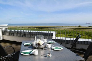 Un espace de restauration en plein air avec vue sur la mer, une table dressée avec des assiettes, des verres et un centre de table décoratif.