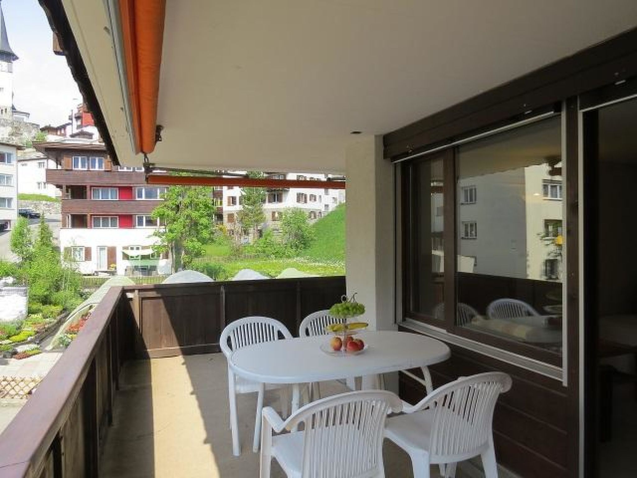 A balcony with a table and chairs, a view of buildings, and a large window.