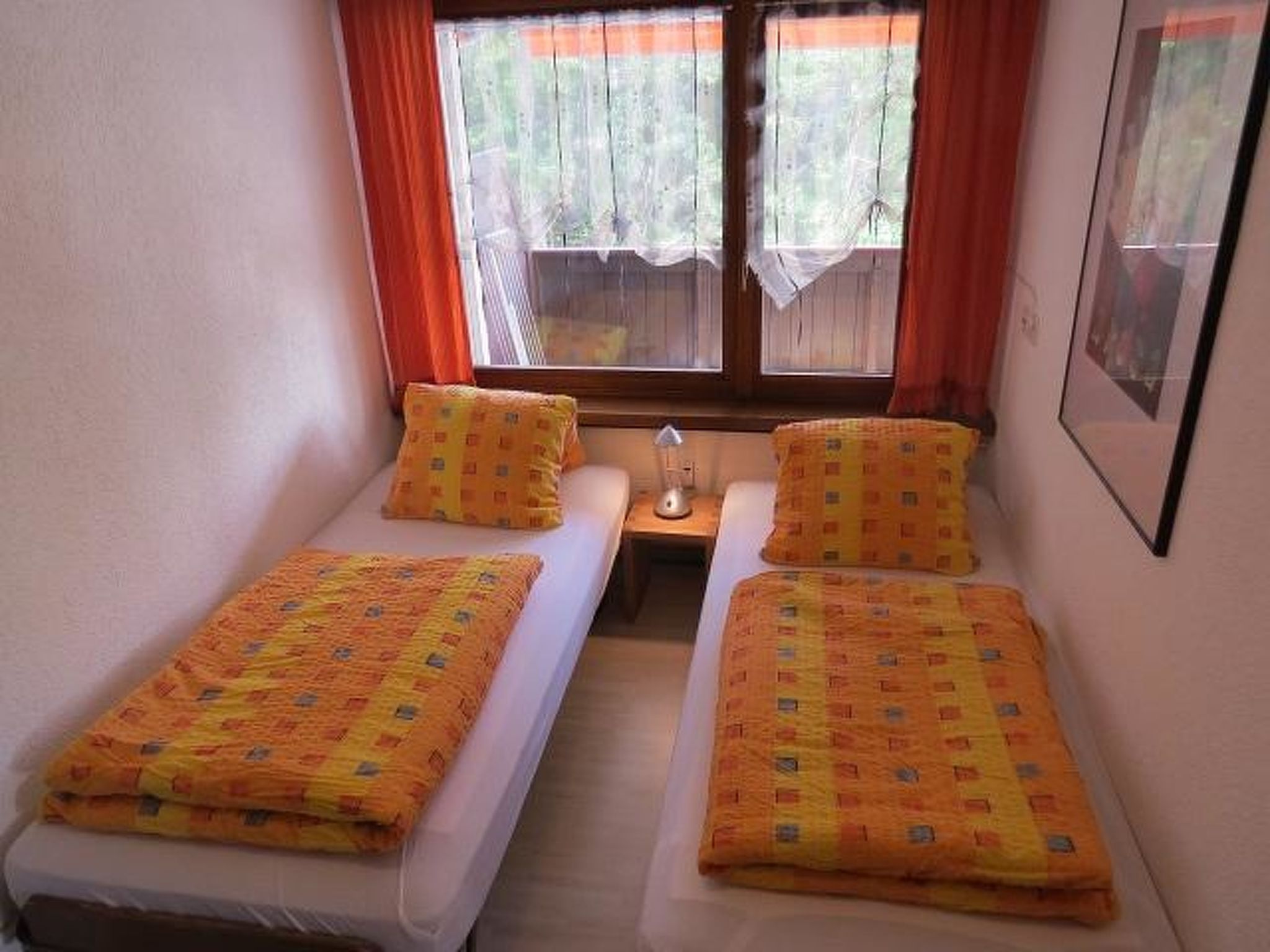 A small room with two single beds, a nightstand, and a window with curtains.
