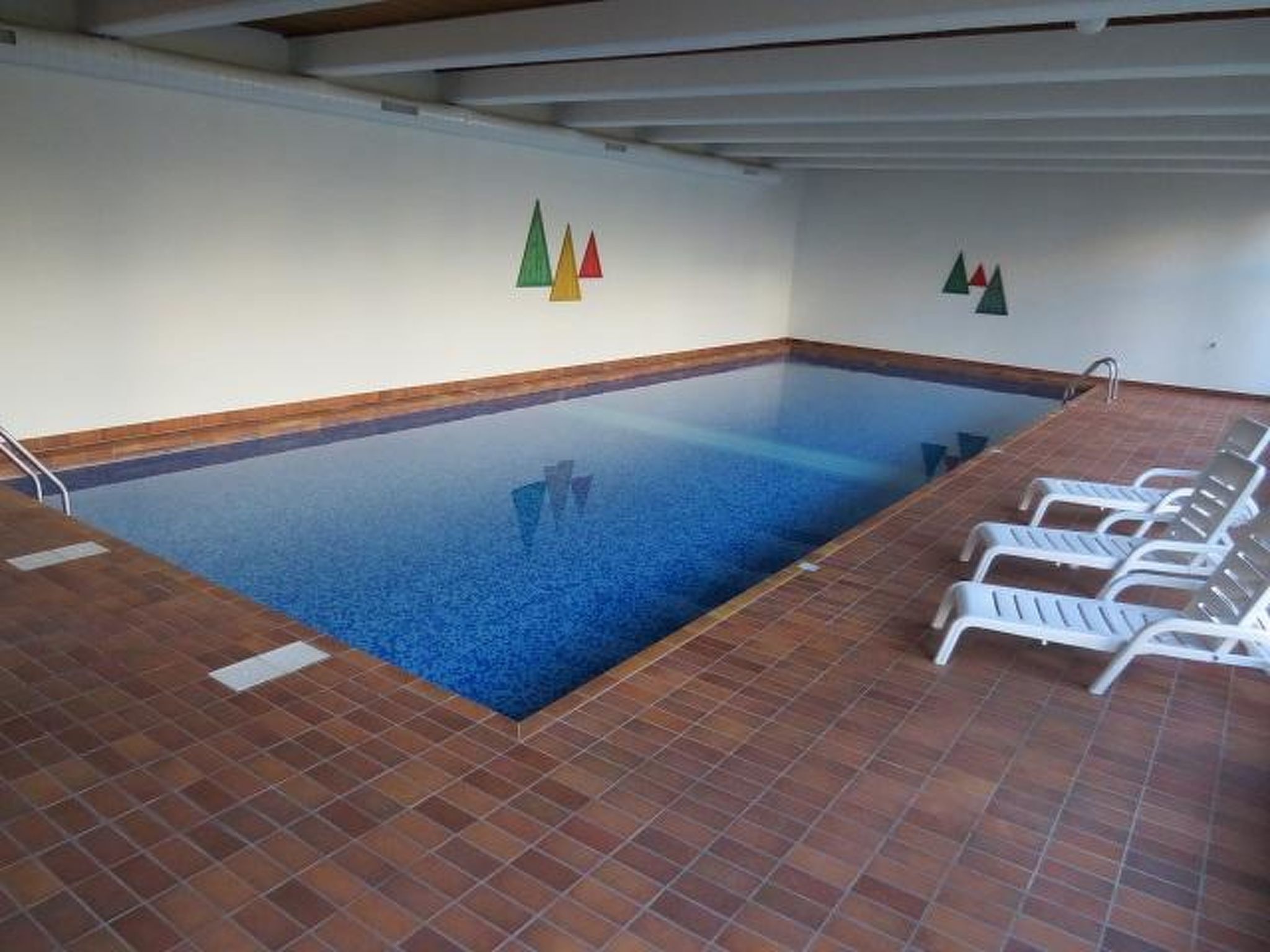 An indoor swimming pool with tiled flooring and white lounge chairs.