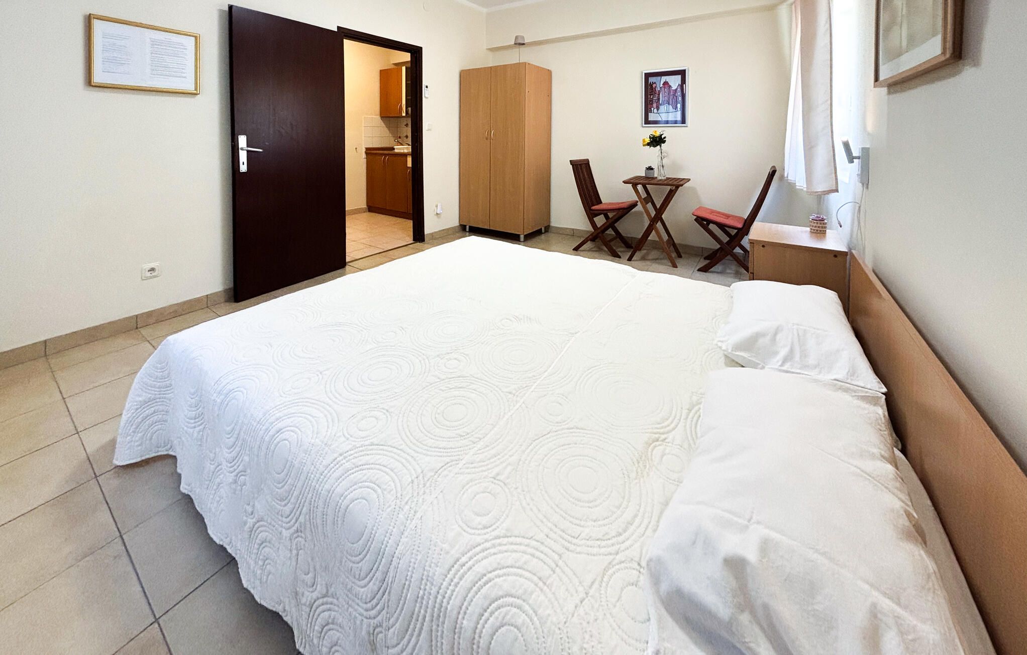 Una habitación de hotel con una cama grande, un armario de madera, una pequeña mesa con sillas y un cuadro en la pared.
