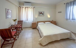 Ein Schlafzimmer mit Bett, Nachttischen, einem Schreibtisch mit Stühlen, einem Fenster mit Vorhängen und einer Wand-Klimaanlage.